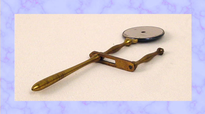 Brass ophthalmoscope with round mirror on the end and a handle attached to the shaft.