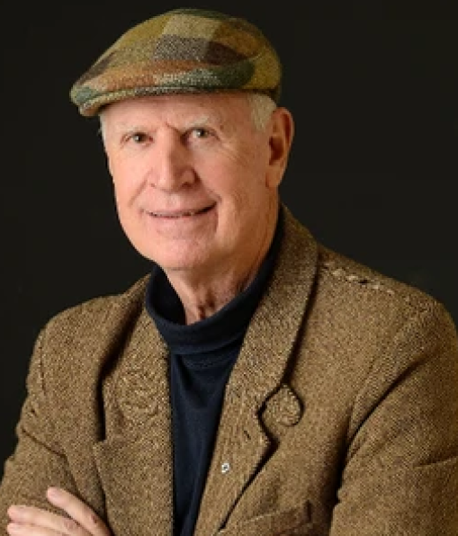 Photograph of Dr. Bill Wall in a brown suit with a checked brown newsboy hat.